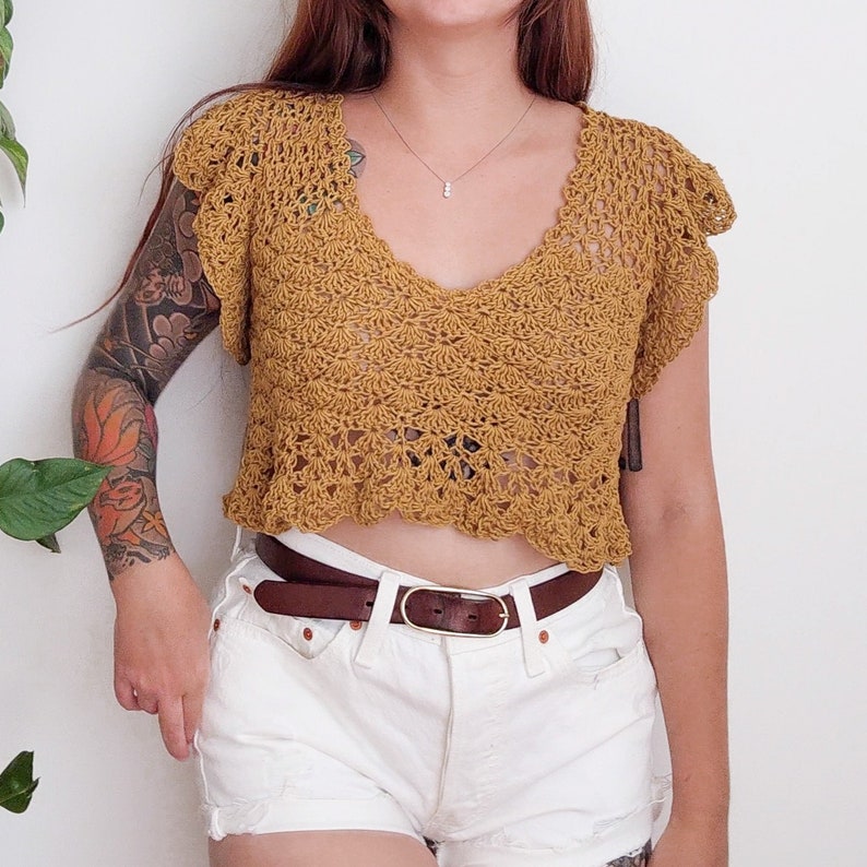 A Yellow Buttercup Top modeled on a woman. This crochet blouse features a deep V neckline, flouncy hem, cropped fit, and flutter sleeves. Made with a linen yarn.