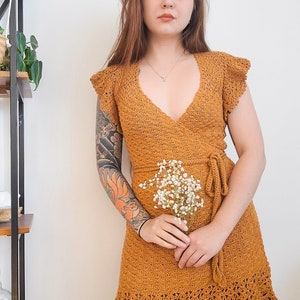 May include: A mustard yellow crochet dress with a V-neckline, short sleeves, and a tie at the waist. The dress has a ruffled hem and is made of a lightweight, breathable fabric.