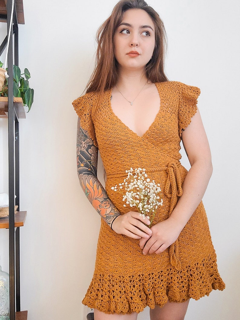 May include: A mustard yellow crochet dress with a V-neckline, short sleeves, and a tie at the waist. The dress has a ruffled hem and is made of a lightweight, breathable fabric.