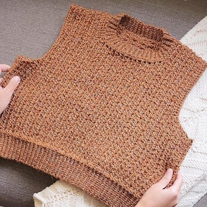 May include: A brown sleeveless knitted jumper with a textured pattern.