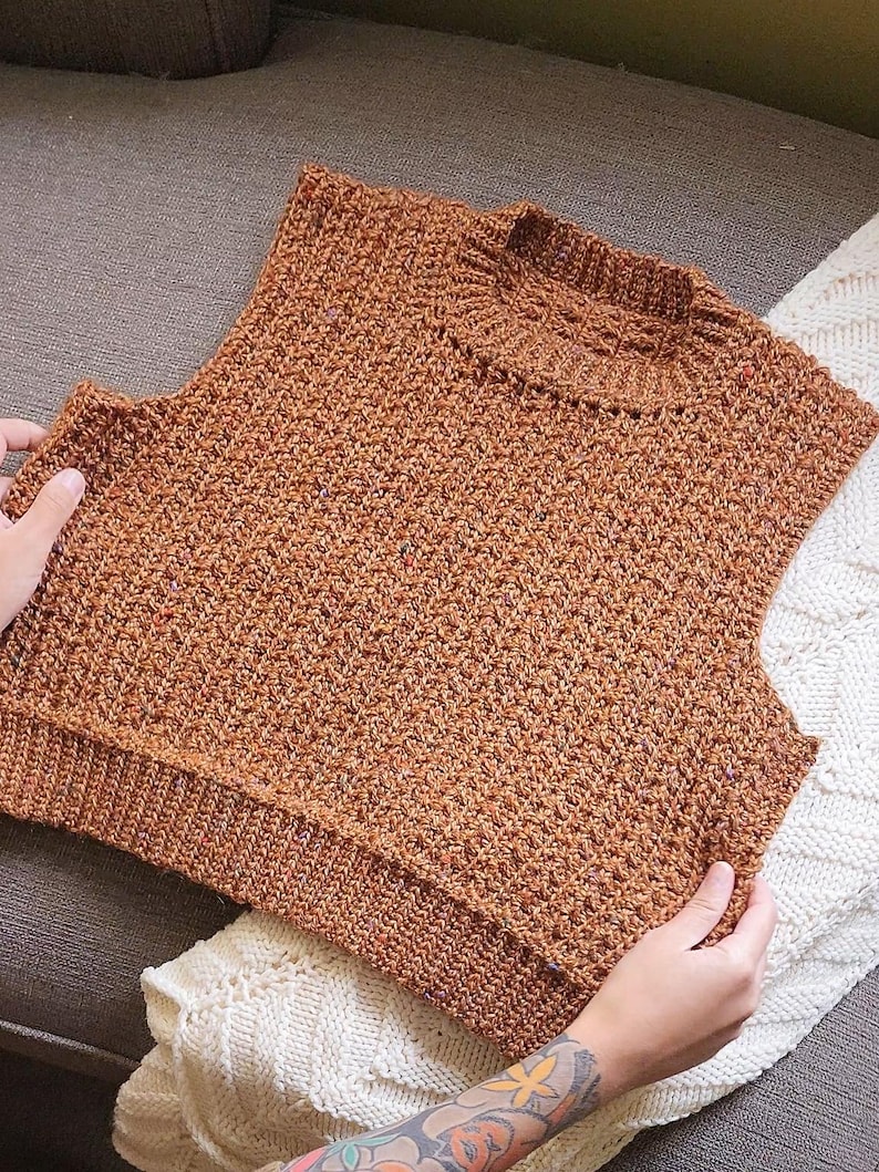 May include: A brown sleeveless knitted jumper with a textured pattern.