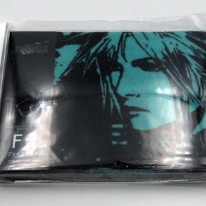 May include: A black face towel featuring a teal and black graphic of a person's face. The towel is packaged in clear plastic. The text "FINAL FANTASY VII REMAKE" is visible on the packaging.