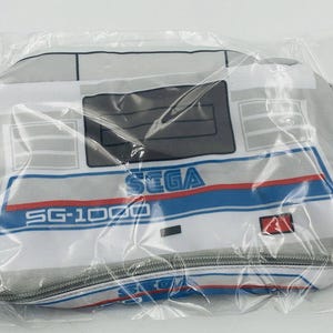 May include: A white and blue Sega SG-1000 video game console zippered pouch. The pouch has a zipper closure and a white background with blue and red stripes. The text "SEGA" and "SG-1000" are printed on the pouch.
