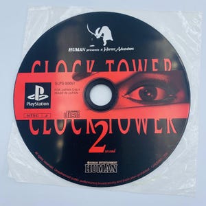 May include: A black PlayStation game disc for "Clock Tower 2" in a plastic sleeve. The disc features red text and an eye graphic. The game is a "Horror Adventure" by Human Entertainment, made in Japan.