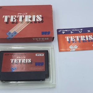 Pode incluir: Um conjunto de video game Tetris vintage, com uma caixa vermelha com o título do jogo em branco e caracteres japoneses. Inclui o cartucho do jogo em uma caixa transparente e um pequeno livreto de instruções. O cartucho é preto.