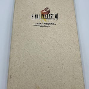 May include: A rectangular, beige, speckled paper-textured case for the Final Fantasy VIII Original Soundtrack. The cover features the game logo, a small illustration of two figures embracing, and text crediting composer Nobuo Uematsu.