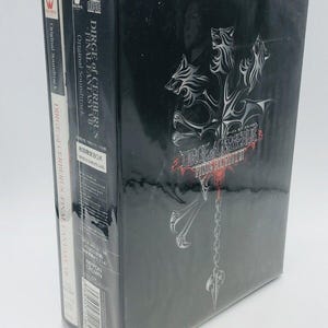 May include: A boxed set of the "Dirge of Cerberus - Final Fantasy VII" video game soundtrack. The black box features a silver graphic of a three-headed wolf and the game title in red. Two soundtrack CDs are visible on the left.