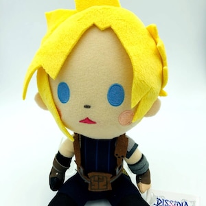 Könnte beinhalten: Ein Plüschtier von Cloud Strife aus der Final Fantasy-Reihe. Das Spielzeug sitzt mit gekreuzten Armen. Es hat gelbes, stacheliges Haar, blaue Augen und einen roten Mund. Das Spielzeug trägt eine blaue Weste und eine braune Hose. Das Spielzeug ist mit "Dissidia Final Fantasy Theatrhythm All-Star Carnival" gekennzeichnet.