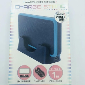 May include: A dark blue charging stand for a New 2DS LL gaming console, packaged in a white box with colourful accents. The box displays the text CHARGE STAND, features a 1-metre USB cable, and illustrates the device's compact design.