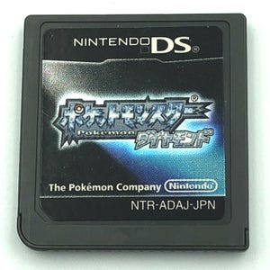 Peut inclure: Cartouche de jeu Nintendo DS noire avec le jeu "Pokémon Diamant". La cartouche porte le logo Nintendo DS en haut et le logo Pokémon au centre. The Pokémon Company et NTR-ADAJ-JPN sont également imprimés.