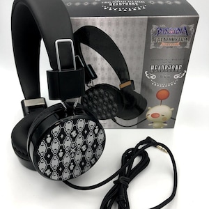 Könnte beinhalten: Schwarze Kopfhörer mit einem weißen und grauen Muster. Die Kopfhörer sind in einer Box verpackt, auf der "Final Fantasy All Stars Headphone" und "Dissidia Theatrhythm All-Star Carnival" steht.