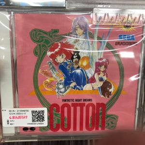 May include: A pink CD case with a colorful illustration of three anime characters. The case features the title "Cotton: Fantastic Night Dreams" and the Sega Success logo. The back of the case includes a barcode and the text "OD#+ 27-0548700 G.S.M.1500シリーズ まんだらけ コットン 0300083304 2700004 (税別 PORT CARTO"