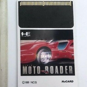 Może przedstawiać: Biała kaseta gry do konsoli Sega Saturn. Kaseta ma na przodzie czerwony i czarny obraz futurystycznego samochodu. Tekst "MOTO ROADER" jest nadrukowany na przodzie kasety srebrnym kolorem. Tekst "HuCARD" jest nadrukowany na przodzie kasety czarnym kolorem.