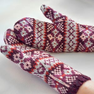 May include: A pair of knitted mittens featuring a complex geometric pattern in shades of deep plum, light pink, grey, and bright orange. The mittens have a ribbed cuff and a thumb section, showcasing a multi-coloured fair isle style knit design.