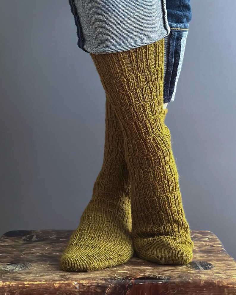 May include: Mustard yellow knitted leg warmers with a textured pattern. The leg warmers are worn with denim shorts. The knitted socks are made of a soft, warm material.