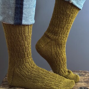 May include: A pair of olive green knitted socks with a textured pattern. The socks are worn with blue jeans. The socks are made of a soft, comfortable material.