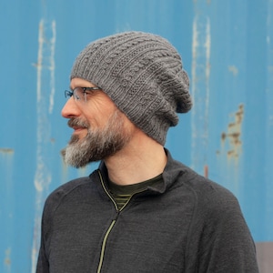 May include: A man wearing a grey knitted beanie with a textured pattern. He is wearing a dark grey zip-up shirt.