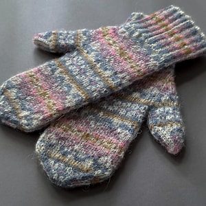 Könnte beinhalten: Ein Paar handgestrickte Fäustlinge mit einem melierten Garnmuster in Blau-, Rosa- und Beigetönen. Die Fäustlinge haben ein geripptes Bündchen und ein strukturiertes, mehrfarbiges Strickmuster, das die gesamte Oberfläche der Hand und des Daumens bedeckt.