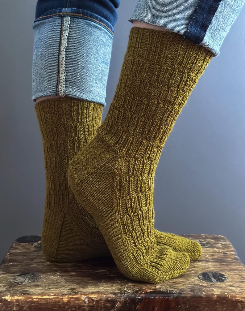 May include: Close-up of mustard-coloured knitted socks with a textured pattern. The socks are worn with blue jeans. The socks are made of a soft, comfortable material.