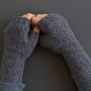 May include: A pair of grey knitted fingerless gloves with a textured diamond pattern. The gloves are made of a soft, warm material and have ribbed cuffs. The gloves are designed to keep hands warm while leaving fingers free.