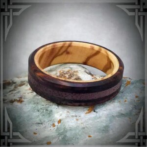 May include: A wooden ring with a light brown wood center and a dark brown wood outer band with a purple stripe.