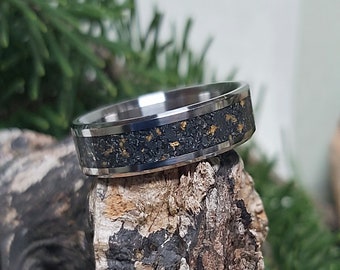 Puede incluir: Un anillo de plata con incrustaciones negras y doradas. El anillo está sobre una pieza de madera.