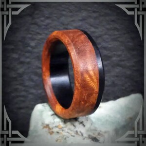 May include: A wooden ring with a black inlay. The wood has a reddish-brown color and a natural grain pattern.
