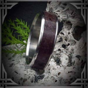 May include: A stainless steel ring with a dark brown inlay. The ring is set against a white, textured background.