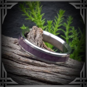 May include: A stainless steel ring with a purple wood inlay. The ring is on a piece of wood.