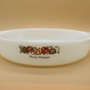May include: White oval casserole dish with handles, featuring a colorful illustration of vegetables and the text "PETITE POTAGER". The dish is made of opaque glass and is suitable for baking and serving.