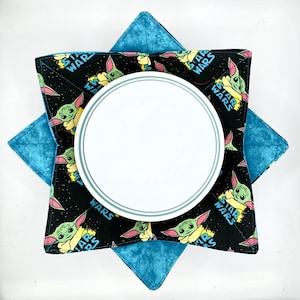May include: A white plate rests on a black and teal hot pad. The hot pad features a Star Wars design with the character Grogu and the words "Star Wars". The hot pad is teal on the bottom.
