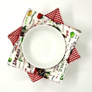 May include: A white ceramic bowl with a red and white gingham bowl cozy. The cozy has a print of various food items and the text "fresh blend diced water into lime tiny cilantro CAMOLE 1 red food cesso 10 onion chili powder lime COWBOY".