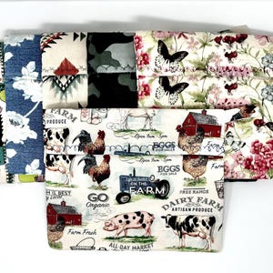 May include: Five fabric panels with different farm-themed prints. The panels are all white with various colors and designs. One panel features a red barn, a rooster, and a pig. Another panel features a tractor and the words "Farm on the Farm". A third panel features a cow and the words "Dairy Farm Artisan Produce". A fourth panel features a cactus and the words "Farm Produce". The fifth panel features a floral design with butterflies.
