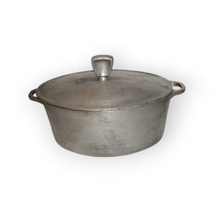 以下が含まれることがあります： 蓋と蓋に小さな取っ手が付いた銀色のアルミ鍋。鍋は楕円形で、表面がわずかにざらざらしている。