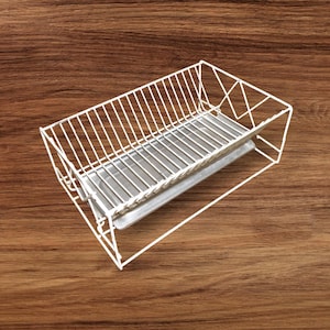 May include: A white wire dish rack with a rectangular shape and a metal tray. The rack is designed to hold dishes and utensils. The rack is made of white metal and sits on a wooden surface.