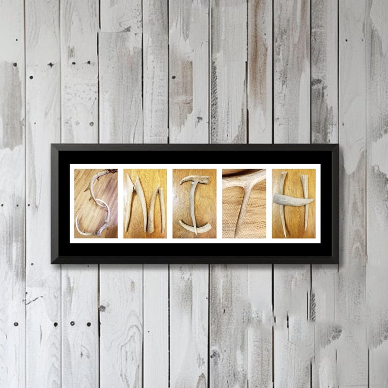 May include: A framed print of the name "SMITH" spelled out using antlers. The antlers are arranged to form the letters of the name. The background is a light wood grain.