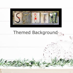 May include: A framed print with the word "SMIT" spelled out using fishing-themed images. The background is a light blue woodgrain pattern. The print is framed in black with a white mat.