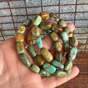 May include: A strand of turquoise beads with a mix of green and brown tones. The beads are oval shaped and have a smooth, polished finish.