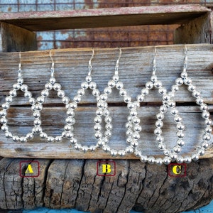 May include: Five pairs of silver hoop earrings with a beaded design. The earrings are hanging from a wooden crate.
