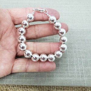 Pode incluir: Uma pulseira de prata com contas grandes e redondas. A pulseira tem um fecho de lagosta.