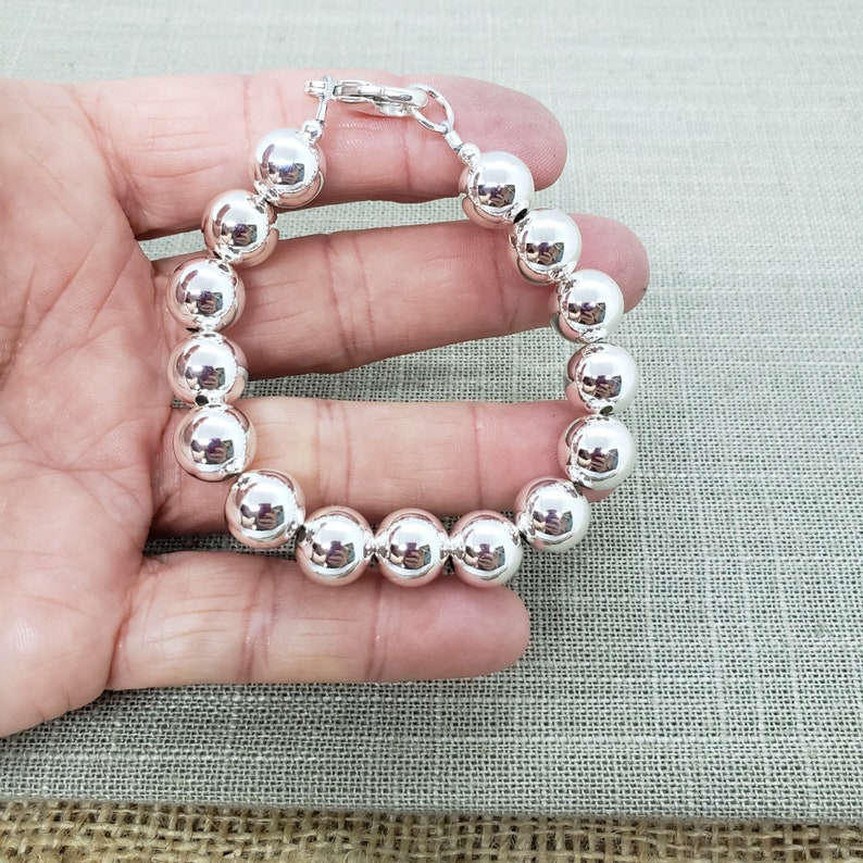 Pode incluir: Uma pulseira de prata com contas grandes e redondas. A pulseira tem um fecho de lagosta.