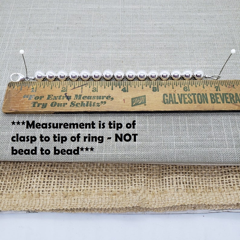 Pode incluir: Um bracelete de prata com contas redondas medido com uma r&eacute;gua de madeira. A r&eacute;gua diz "For Extra Measure, Try Our Schlitz" e "GALVESTON BEVERA". O texto abaixo da r&eacute;gua diz "***Measurement is tip of clasp to tip of ring - NOT bead to bead***".