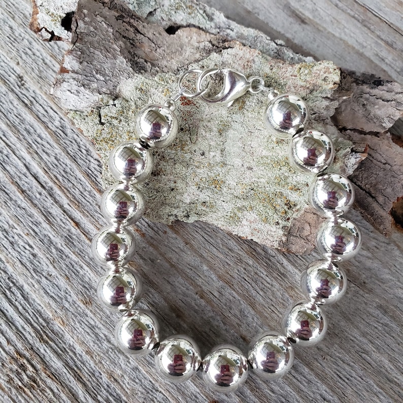 Pode incluir: Um bracelete de prata com fecho de encaixe e grandes contas redondas.