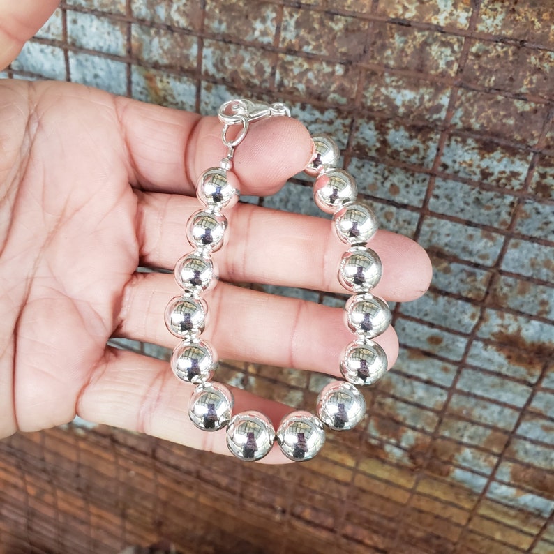 Pode incluir: Um bracelete de prata com fecho de corrente e grandes contas redondas.