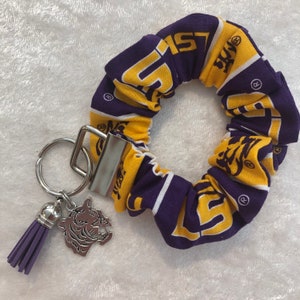 May include: Purple and gold fabric hair scrunchie with a LSU logo and a silver keychain with a purple tassel and a silver tiger charm.
