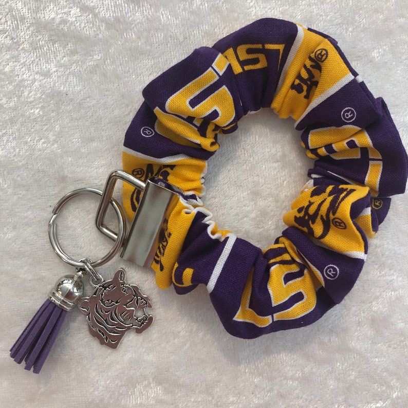 May include: Purple and gold fabric hair scrunchie with a LSU logo and a silver keychain with a purple tassel and a silver tiger charm.