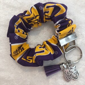 May include: Purple and gold fabric scrunchie with a tiger logo and a silver keychain with a tiger charm and a purple tassel.