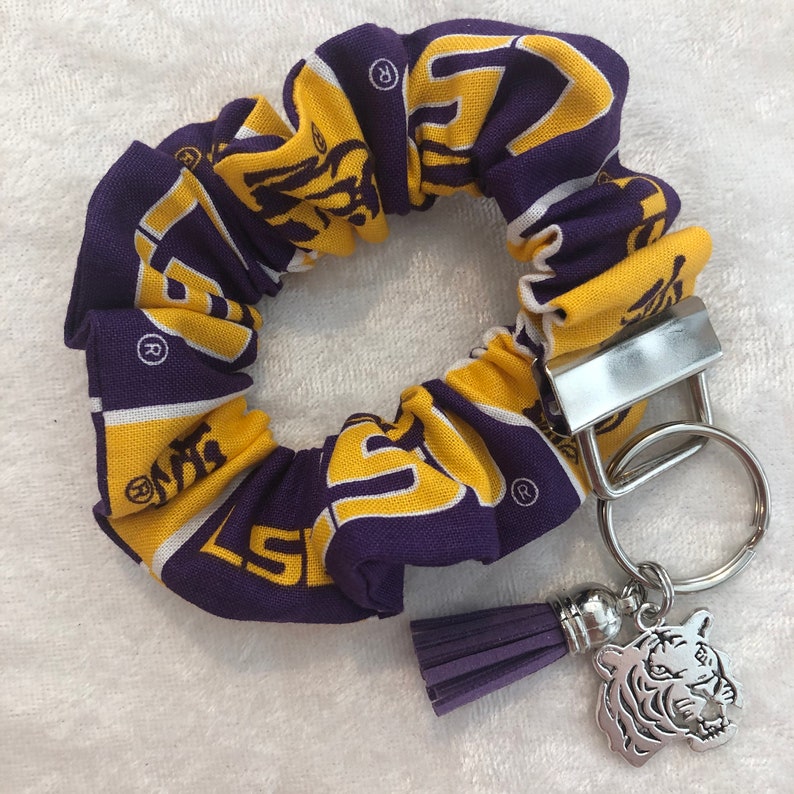 May include: Purple and gold fabric scrunchie with a tiger logo and a silver keychain with a tiger charm and a purple tassel.