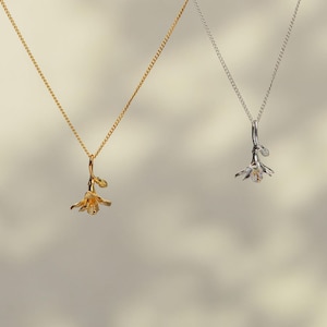 May include: Two delicate necklaces with flower pendants. One necklace is gold and the other is silver.