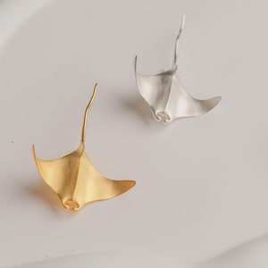 Puede incluir: Dos pendientes con forma de raya, uno dorado y otro plateado, sobre un fondo blanco.